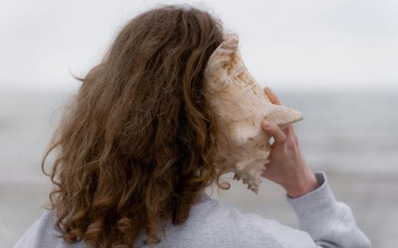 woman holds large shell to her ear