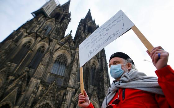 An older person carries a sign and wears a mask outside a cathedral