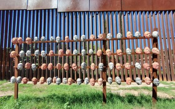 Sculpted papier-maché faces hang on the border wall in Nogales Sonora, Mexico. (Courtesy of Eileen McKenzie)